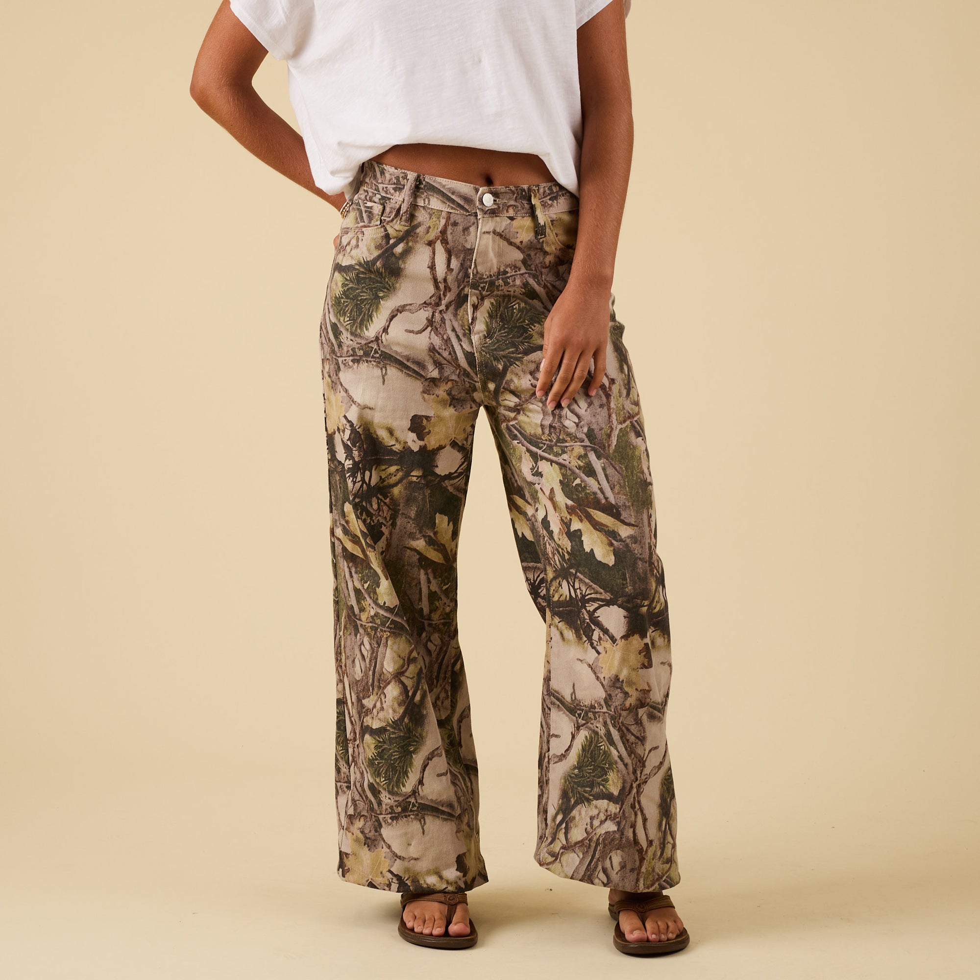 Front view of wide leg camo pants with button closure and relaxed silhouette, styled with white cropped tee.