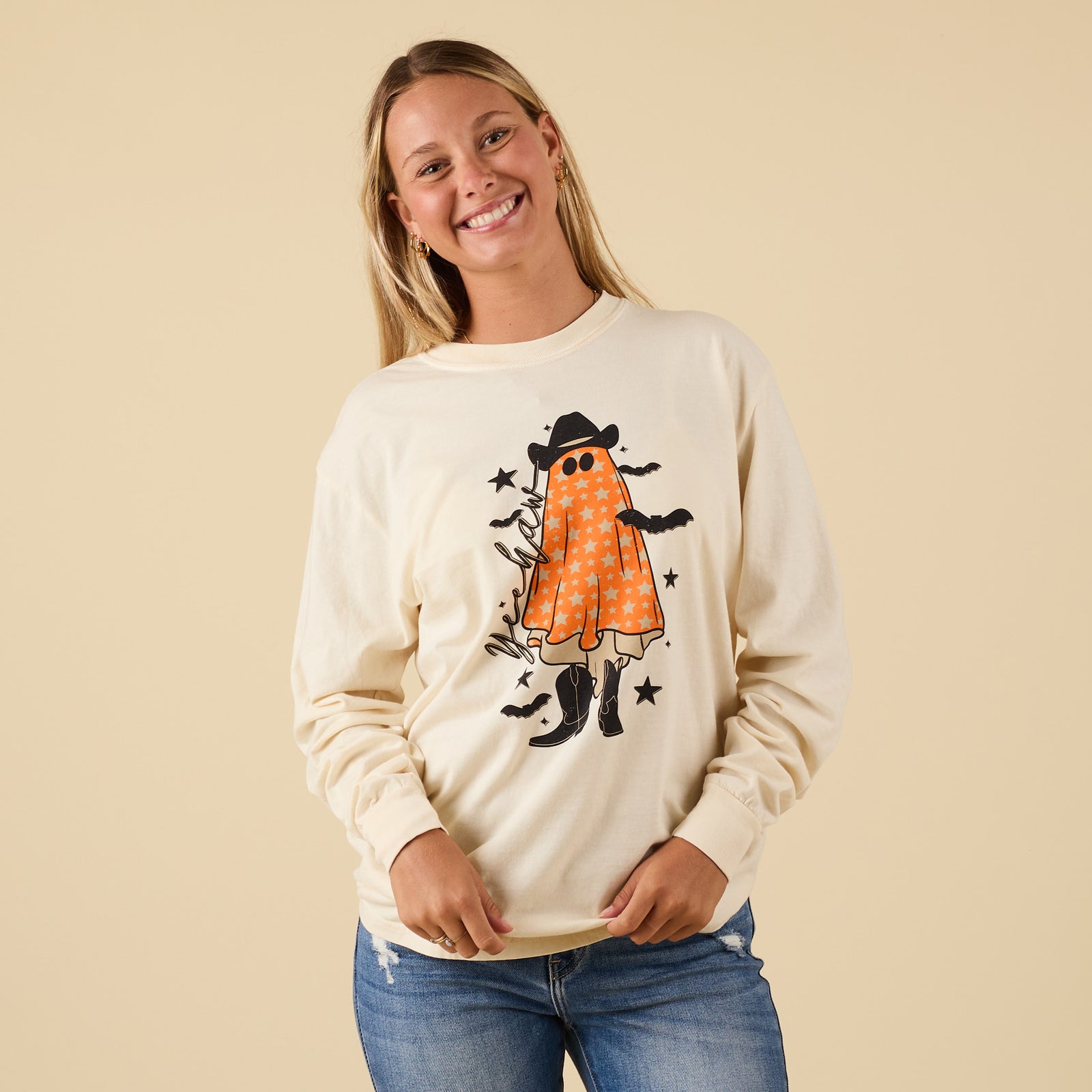 Front view of ivory long sleeve t-shirt with orange star-print ghost wearing cowboy hat and boots, with bats and stars around design.