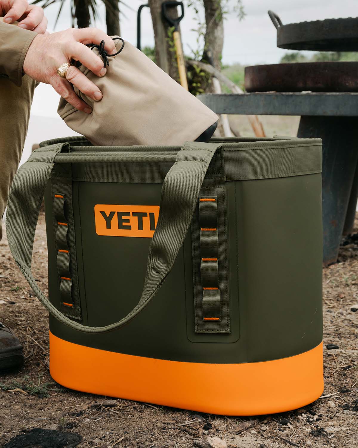 Someone putting something into a olive yeti camino bag.