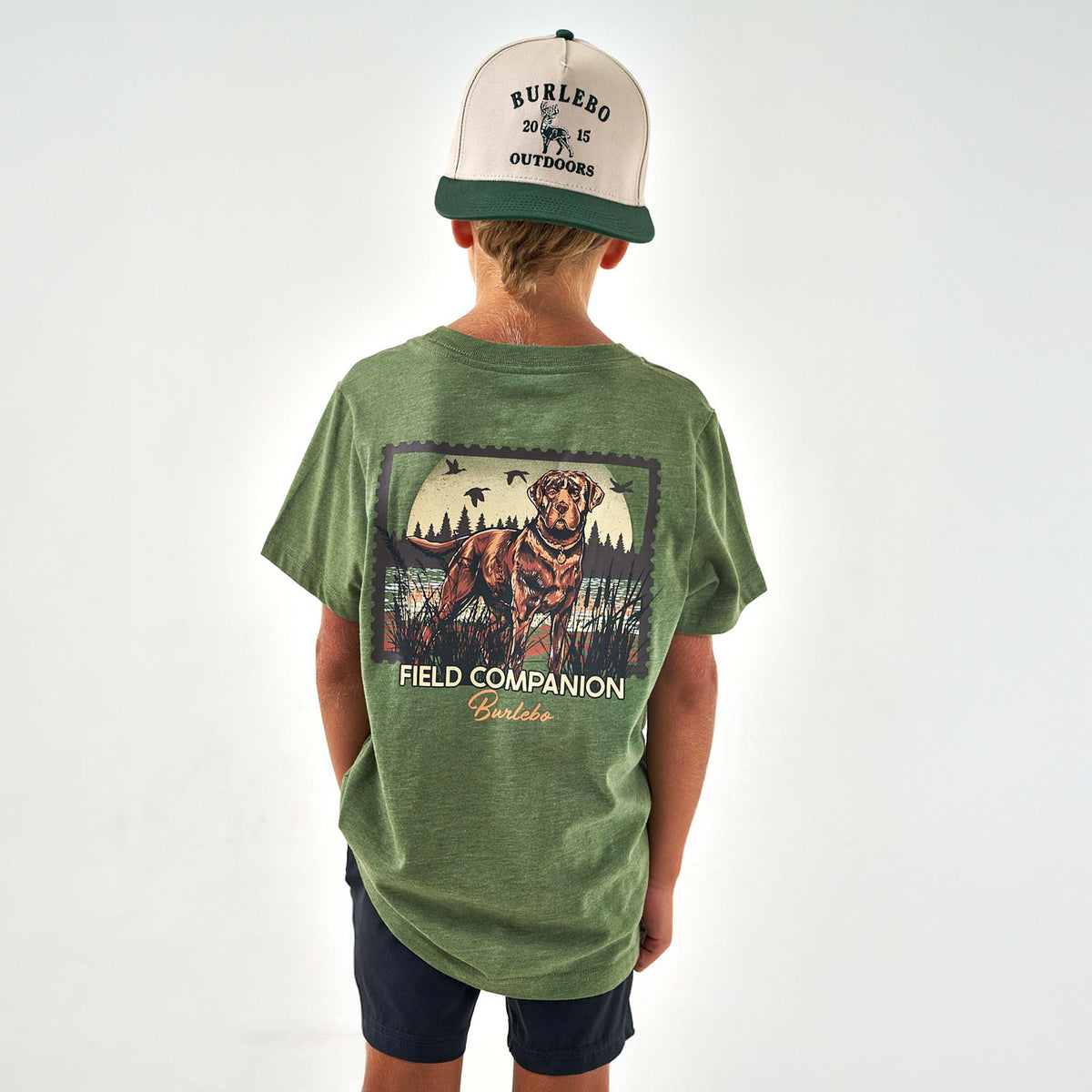 Person wearing a green t-shirt with a graphic and text, and a cap on a white background