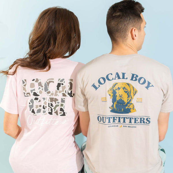 Two models shown from behind wearing graphic T-shirts, one pink and one tan, against a light blue background.